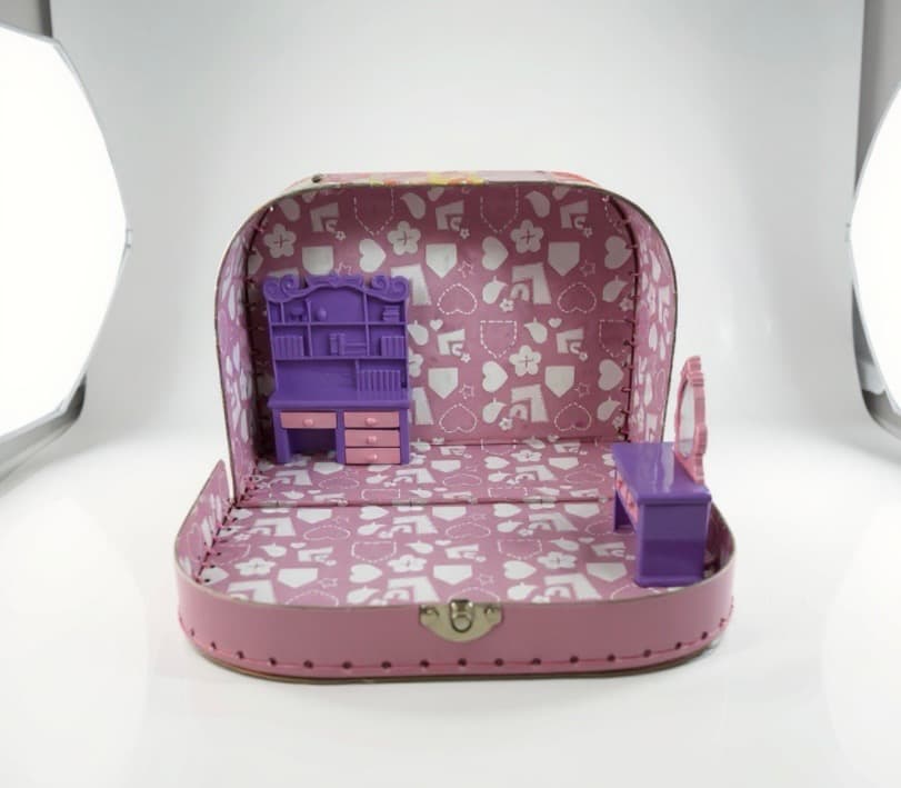 Inside the suitcase: a purple-and-pink miniature dresser with hutch stands against the back wall. A purple vanity table sits to the right. The floor is still bare.