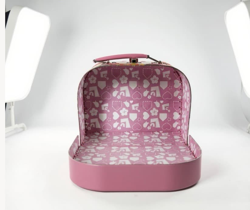 The same suitcase, opened. Lid stands tall. Interior is a soft pink lining with a tiny heart and flower pattern. Completely empty.