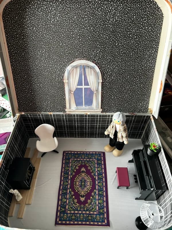 Miniature lounge scene in a suitcase with piano, chair, and lamp.
