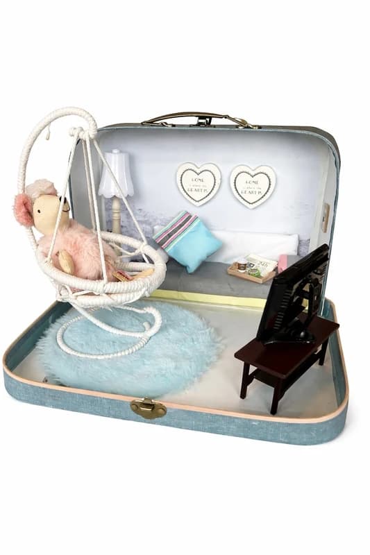 A miniature lounge scene featuring a hanging swing chair, soft textiles, in a tiny suitcase setup.