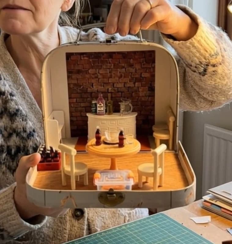 Miniature mini pub scene inside a suitcase, with bar, stools, and bottles.