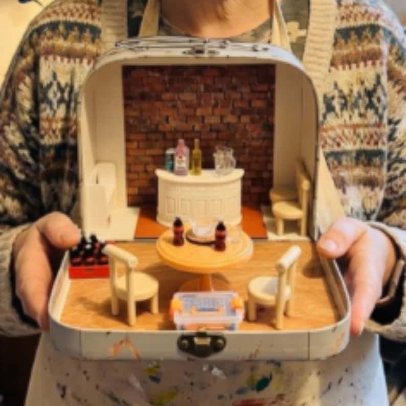 Miniature pub diorama in a suitcase with bar, bottles, and stools.